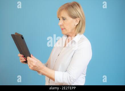 Ältere Frau mit digitalem Tablet auf blauem Hintergrund. Stockfoto
