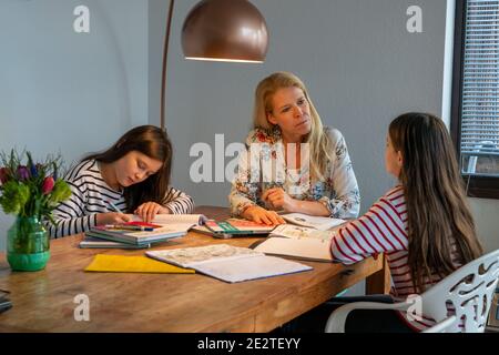Homeschooling, während der Aussperrung im Januar 2021, Mutter hilft ihren beiden Töchtern, zu Hause, zu lernen, Schulschließungen, Fernunterricht, Auswirkungen der Stockfoto