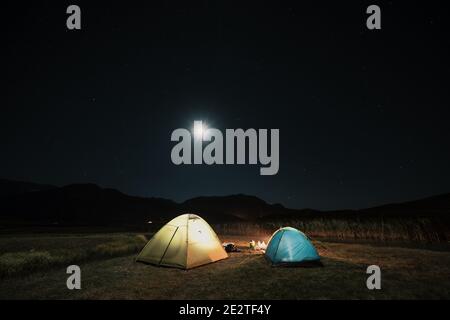 Camping in den Bergen unter dem Mond. Ein Zelt aufgeschlagen und unter dem Himmel glühend. Stockfoto