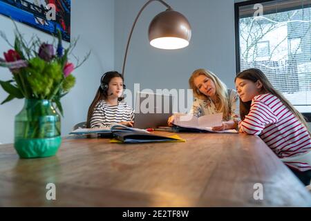 Homeschooling, während der Aussperrung im Januar 2021, Mutter hilft ihren beiden Töchtern, zu Hause, zu lernen, ein Mädchen ist in Video-Unterricht mit ihrer Klasse, sc Stockfoto