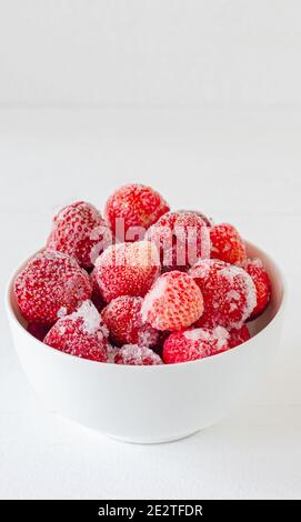 Gefrorene Erdbeere in weißer Schüssel auf einem Holztisch. Beeren mit Reif bedeckt. Stockfoto