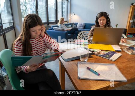 Homeschooling, während der Januar 2021 Sperre, Kinder zu Hause für die Schule studieren, ihre Mutter im Heimbüro arbeiten auf dem Laptop mit vide Stockfoto