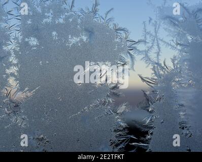 Frostmuster am Fenster mit Blick auf den Sonnenuntergang im Freien hinter Kristalle Stockfoto