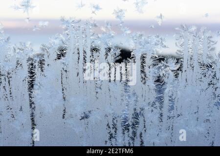 Frostmuster am Fenster mit Blick auf den Sonnenuntergang im Freien hinter Kristalle Stockfoto