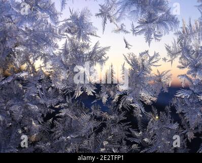 Frostmuster am Fenster mit Blick auf den Sonnenuntergang im Freien hinter Kristalle Stockfoto