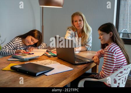 Heimschooling, während der Aussperrung im Januar 2021, Mutter hilft ihren beiden Töchtern, zu Hause, zu lernen, mit Lehrbüchern und Computern, Schulschließungen, Stockfoto