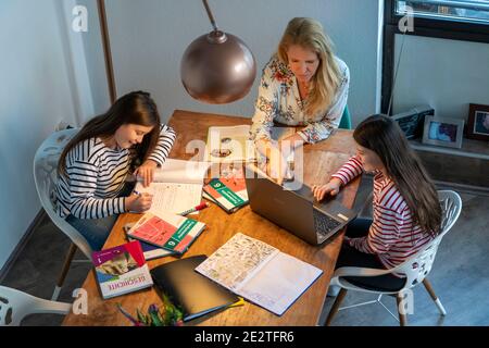 Heimschooling, während der Aussperrung im Januar 2021, Mutter hilft ihren beiden Töchtern, zu Hause, zu lernen, mit Lehrbüchern und Computern, Schulschließungen, Stockfoto