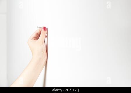 Gepflegte Hand einer jungen Frau, die einen Nagel in die Wand hält, um ihn zu hämmern. Helles Bild mit Kopierbereich. Stockfoto