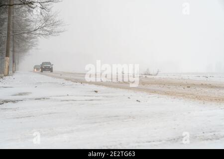 Zwei Autos fahren auf einer schneebedeckten Straße bei Schneefall und Nebel Stockfoto