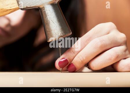 Junge Frau mit gepflegten Händen Nageln einen Nagel in ein Holzbrett mit einem Hammer. Stockfoto