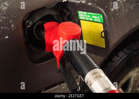 Rote Tankpistole im Kraftstofftank eines schmutzigen, verschneiten Autos an einer Tankstelle in Nahaufnahme. Stockfoto