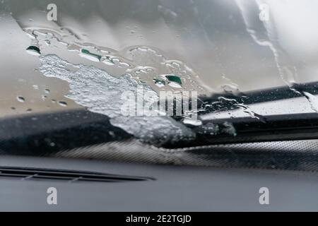 Aufgetautes Eis auf der Windschutzscheibe des Autos in der Nähe der Scheibenwischer bei nassem, schlammigem Wetter. Foto aus dem Auto Stockfoto