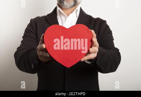 Geschäftsmann in Anzug gekleidet und hält ein rotes Herz auf weißem Hintergrund. Alles Liebe zum Valentinstag Stockfoto