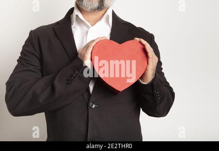 Geschäftsmann in Anzug gekleidet und hält ein rotes Herz auf weißem Hintergrund. Valentinstag Stockfoto