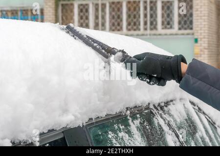 Frau Hand reinigt das Auto von einer großen Menge von Schnee mit einer Bürste Nahaufnahme. Stockfoto