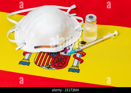 Spanien Flagge, n95 Gesichtsmaske, Nadelspritze und Fläschchen. Konzept der Covid-19 Coronavirus-Impfstoffverteilung, Versorgungsengpässe und Gesundheitskrise Stockfoto