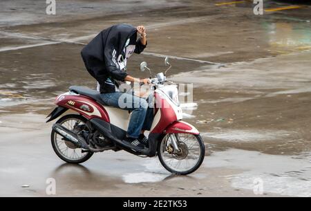 SAMUT PRAKAN, THAILAND, JULI 21 2020, EIN Mann fährt ein Motorrad und schützt sich vor dem Regen mit eigener Jacke Stockfoto