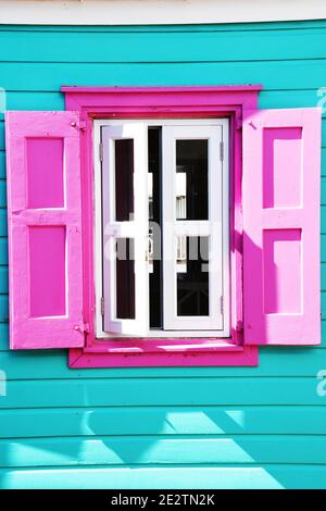 Pinke Fensterläden, weiße Fenster und türkisfarbenes karibisches Gebäude Stockfoto