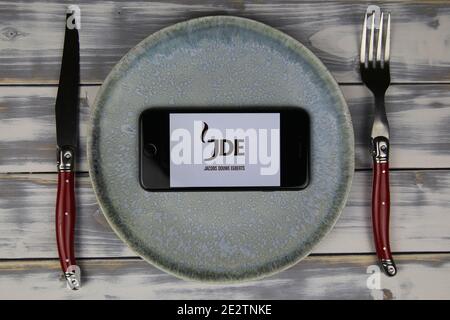 Viersen, Deutschland - 9. Mai. 2020: Nahaufnahme des Mobiltelefons auf Teller und Holztisch, Besteck mit Logo-Schriftzug von jde jacobs douwe egberts Kaffee Essen c Stockfoto