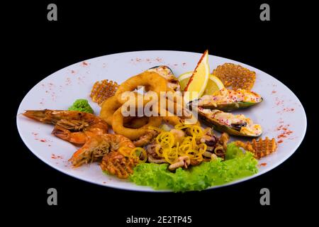 Große Auswahl an frittierten Meeresfrüchten Snacks. Gefüllte Muscheln, panierte Tintenfischringe, Seecocktail, Riesengarnelen mit Zitrone. Nahaufnahme auf einer weißen Platte auf Blac Stockfoto