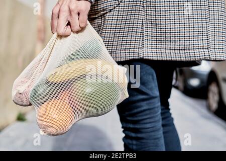 Nahaufnahme eines Mannes auf der Straße, von hinten gesehen, der eine wiederverwendbare Textiltasche trägt, die verwendet wird, um Lebensmittel in großen Mengen zu kaufen, voller Obst und Gemüse, als ich Stockfoto