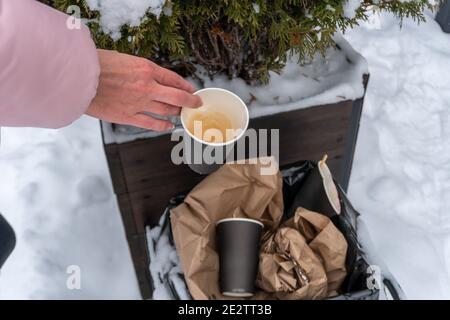 Gebrauchte Kaffeetasse in der Mülleimer weibliche Hand wirft Müll, kümmert sich um die Natur Stockfoto