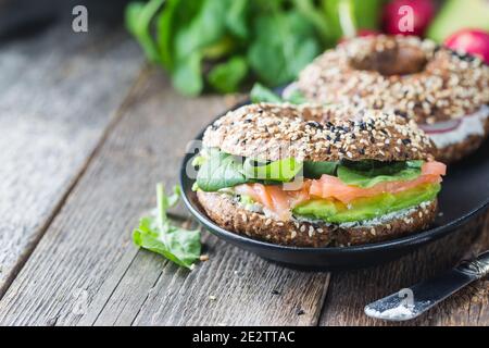 Bagels mit Frischkäse, Avocado, Fisch, Rucola und Radieschen auf alten Holztisch. Gesundes Frühstück zu essen. Stockfoto