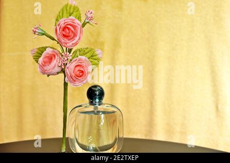 Ein Bouquet von rosa künstlichen Rosen und eine Flasche Parfüm auf gelbem Hintergrund Stockfoto