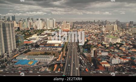 Verkehrsautobahn an modernen Wolkenkratzern Luftaufnahme. Epische Stadtlandschaft mit Straßen entlang der Straße. Blockgebäude und Hütten an bewölktem Sommertag. Downtown Nahverkehr in Manila City, Philippine Stockfoto