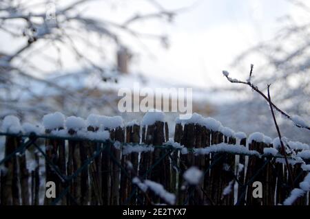 Schöne saisonale ländliche Aussicht. Eine Winterschichtabdeckung aus weißem Daunendeckungszaun und Hausdach. Stockfoto