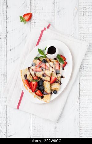 Hausgemachte Crepes-Suzette, leckere Pfannkuchen mit Schokoladensauce, frische Erdbeere und Honig zum Frühstück. Draufsicht Stockfoto