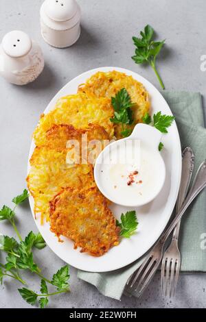 Draniki - Kartoffel-ritters, vegetarische Kartoffelpfannkuchen, serviert mit frischen Kräutern und Knoblauch-Joghurt-Sauce auf altem Hintergrund. Draufsicht. Stockfoto