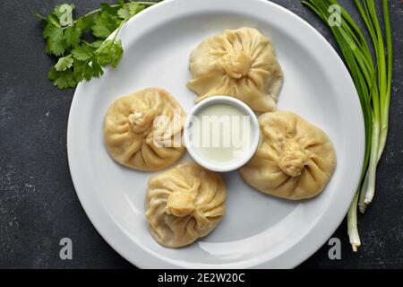 Gekochte Khinkali auf dunklem Grund mit Sauce und Kräutern Stockfoto