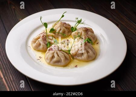 Khinkali auf einem weißen Teller, auf einem hölzernen Hintergrund mit Mikrogrün. Dunkler Holzhintergrund. Stockfoto