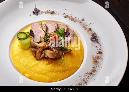 Maisbrei mit Fleisch und Pilzen, auf einem weißen Teller. Polenta, Ugali, Banosh, Mamaliga Stockfoto