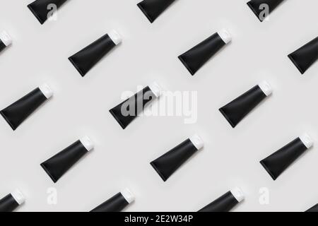 Ein Muster aus schwarzen cremefarbenen Röhren auf hellgrauem Hintergrund. Kosmetische Produkte für die Pflege der Haut von Gesicht, Händen, Füßen und Körper. Stockfoto