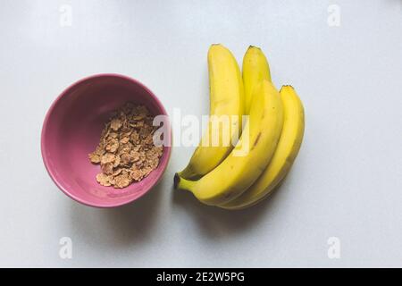Rosafarbene Schale mit Cornflakes und gelben Bananen, Draufsicht Stockfoto