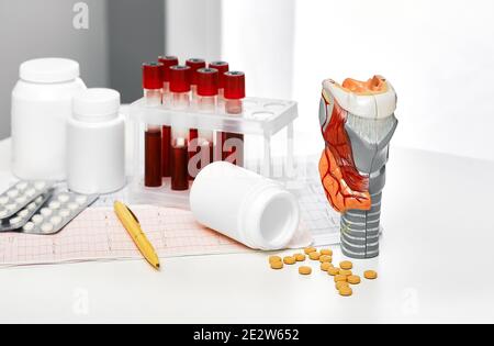 Anatomisches Modell der Schilddrüse, Blut für die Analyse in Reagenzgläsern und Pillen für die endokrinologische Behandlung, Nahaufnahme. Diagnose von Schilddrüsenerkrankungen Stockfoto