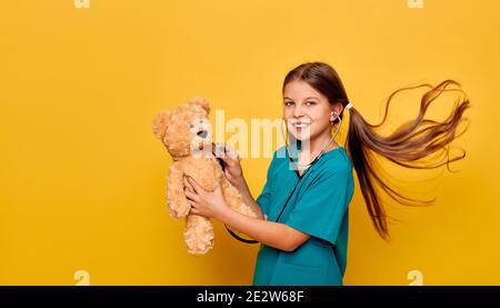 Lächelndes Mädchen trägt in einer medizinischen Uniform spielen Arzt und Hören Sie ihrem Patienten Plüschbären mit Phonendoskop zu Stockfoto