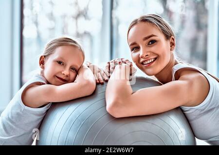 Portrait der jungen attraktiven Frau mit ihrer kleinen Tochter auf fit Ball auf Ausbildung lächelnd aussehende Kamera. Happy Healthy Familienkonzept Stockfoto