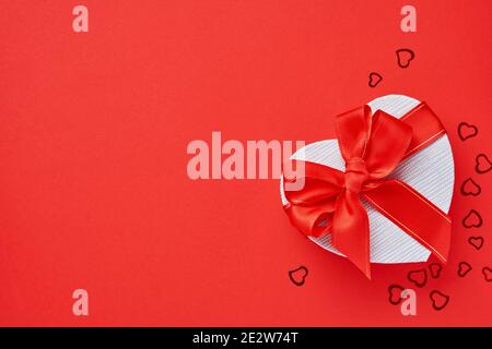 Geschenkbox in Herzform mit rotem Band auf rotem Hintergrund. Valentinstag Konzept Postkarte. Draufsicht. Stockfoto
