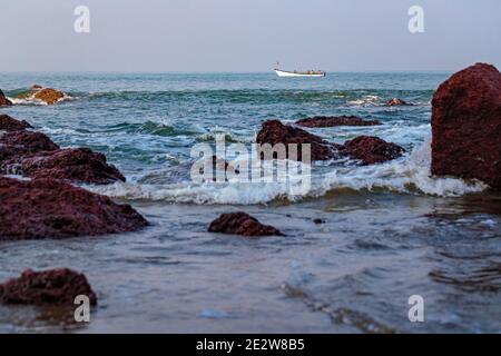 Morgendliches Seascape. Schöne Klippen in Ufernähe und ein Fischerboot. Fischer fangen am frühen Morgen Fisch. Arambol, Goa, Indien Stockfoto