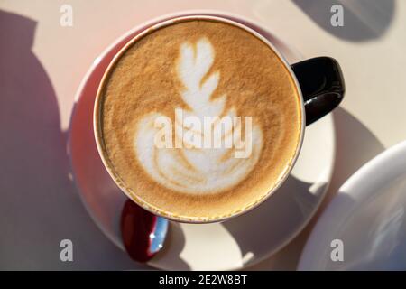 Tasse Cappuccino, Latte Art Design, Zeichnung auf Schaum, Nahaufnahme, auf einem Tisch in einem Straßencafé an einem sonnigen Tag. Konzept heiße Getränke, Kuhmilchersatz Stockfoto