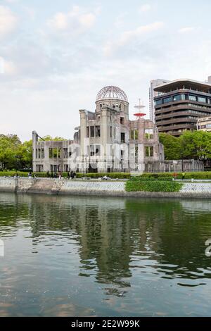 Hiroshima Friedensdenkmal, über den Fluss gesehen und reflektiert, mit der Stadt hinter sich und Menschen, die vorbeigehen, Hiroshima, Japan Stockfoto