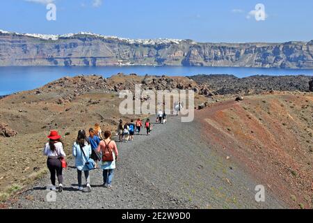 Touristen, die über den aktiven Vulkan von Santorini auf der Insel Nea Kameni wandern. Im Hintergrund befindet sich die Caldera von Santorini. Stockfoto