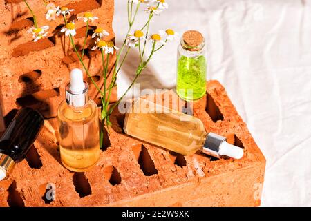Rote Ziegel Podium für die Werbung Kosmetik-Produkte mit Kamillenblumen. Glas Essenz oder feuchtigkeitsspendende Serum und Kamille. Hinterer Stoff in Beige Stockfoto