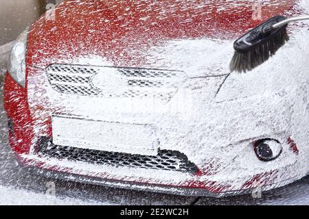 Rotes Auto gewaschen in selbst dienen Autowäsche, Detail auf weißem Seifenschaum Sprühen aus Hochdruckschlauch, Abdeckung alle vorderen Stoßfänger und Kennzeichen Stockfoto