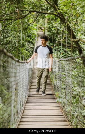 Junger hispanischer Mann, der auf einer Hängebrücke in der geht Mitten im Wald - junger Reisender, der beim Beobachten spazierengeht Natur und genießen Sie die Fahrt - Stockfoto