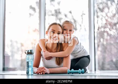 Happy Little girl umarmt ihre schöne sportliche Mutter beim Liegen Matten auf Training. Gesundes Lifestyle-Konzept Stockfoto