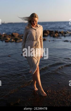 Eine schwangere Frau geht im Sommer an der Küste entlang. Stockfoto